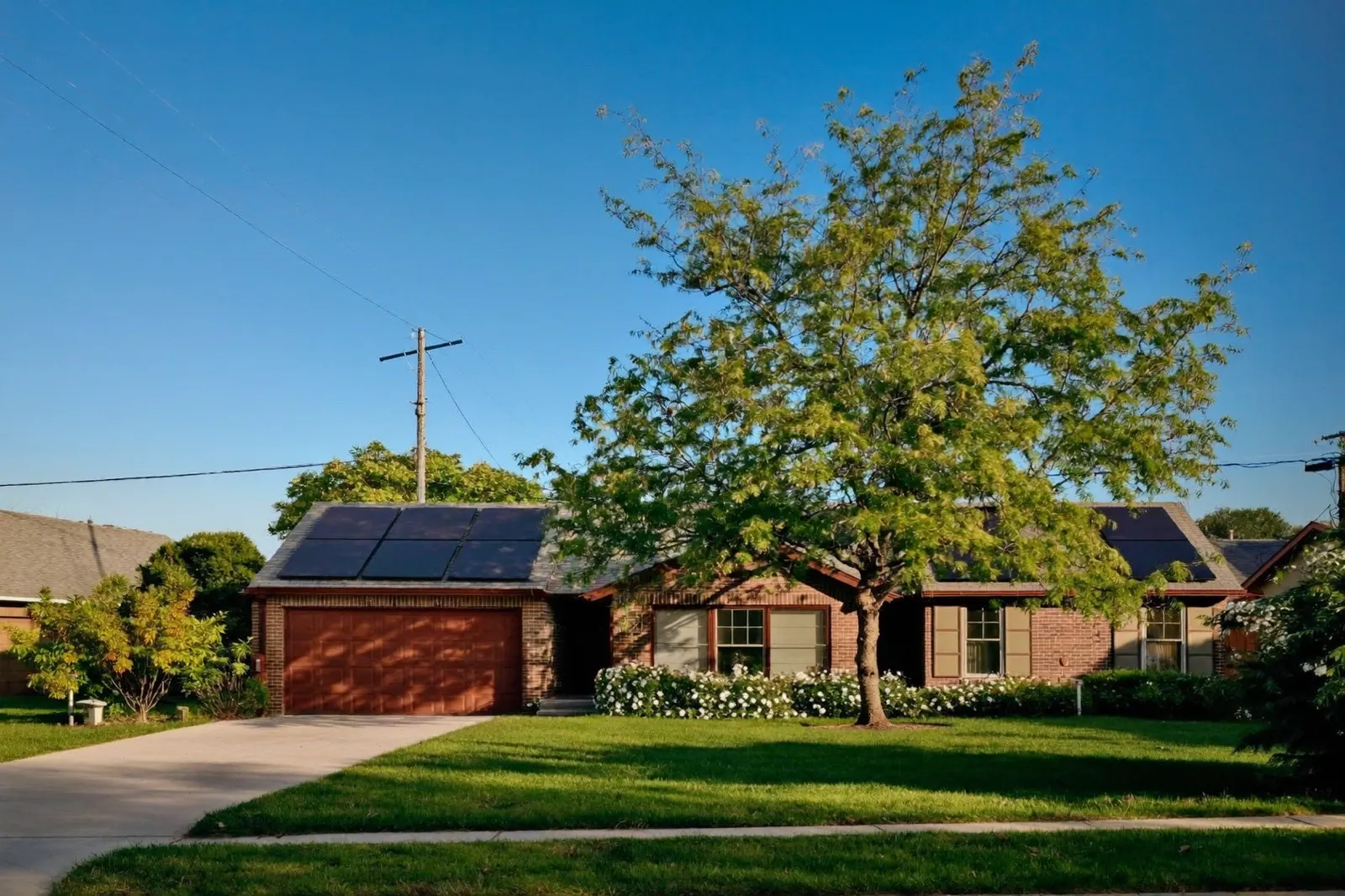 A single-storey brick bungalow in afternoon sun with black solar panels on its south and east roof faces